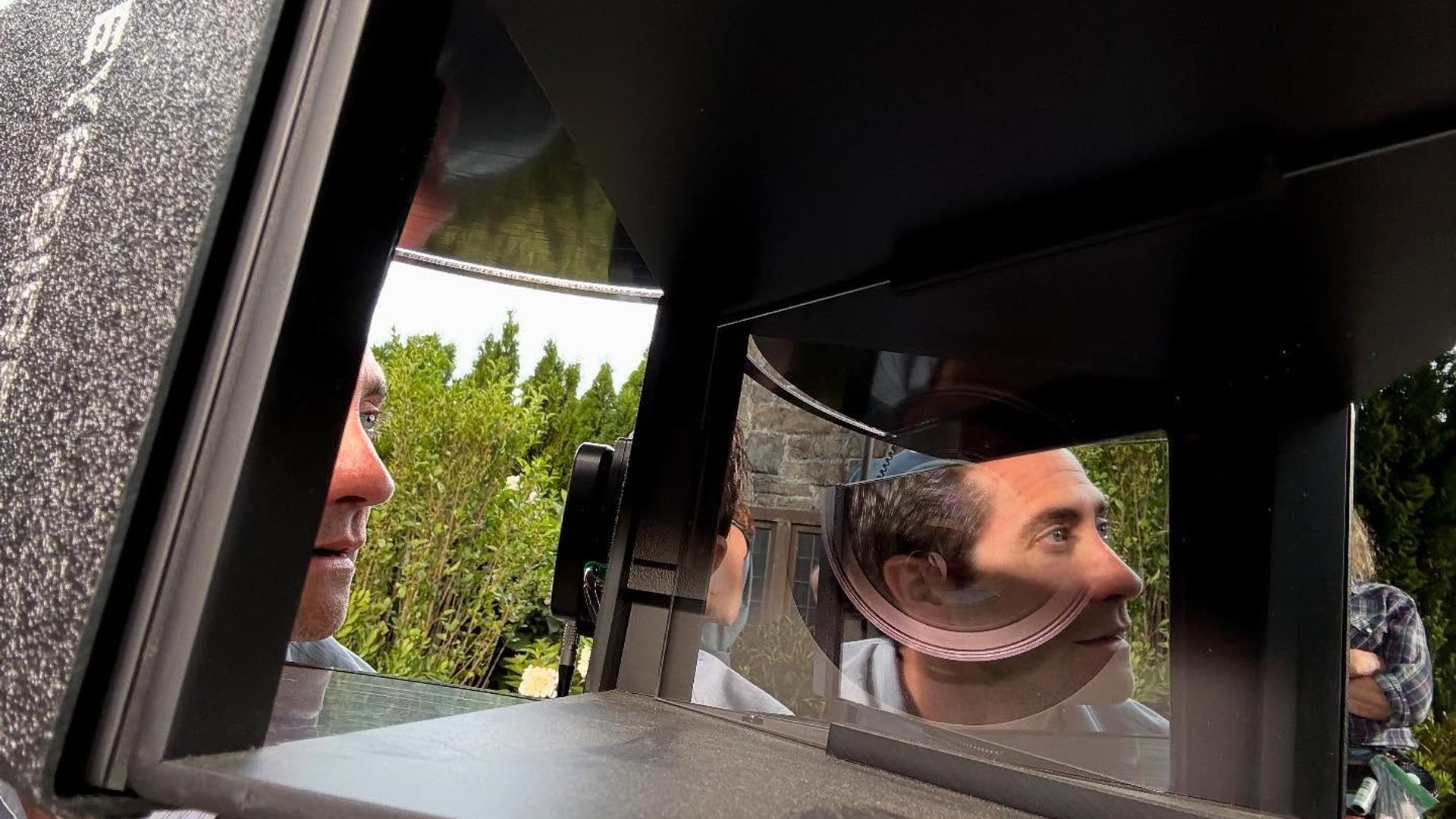 Jake Gyllenhaal mira hacia un equipo con espejos y lentes, su rostro reflejado en las superficies ópticas
