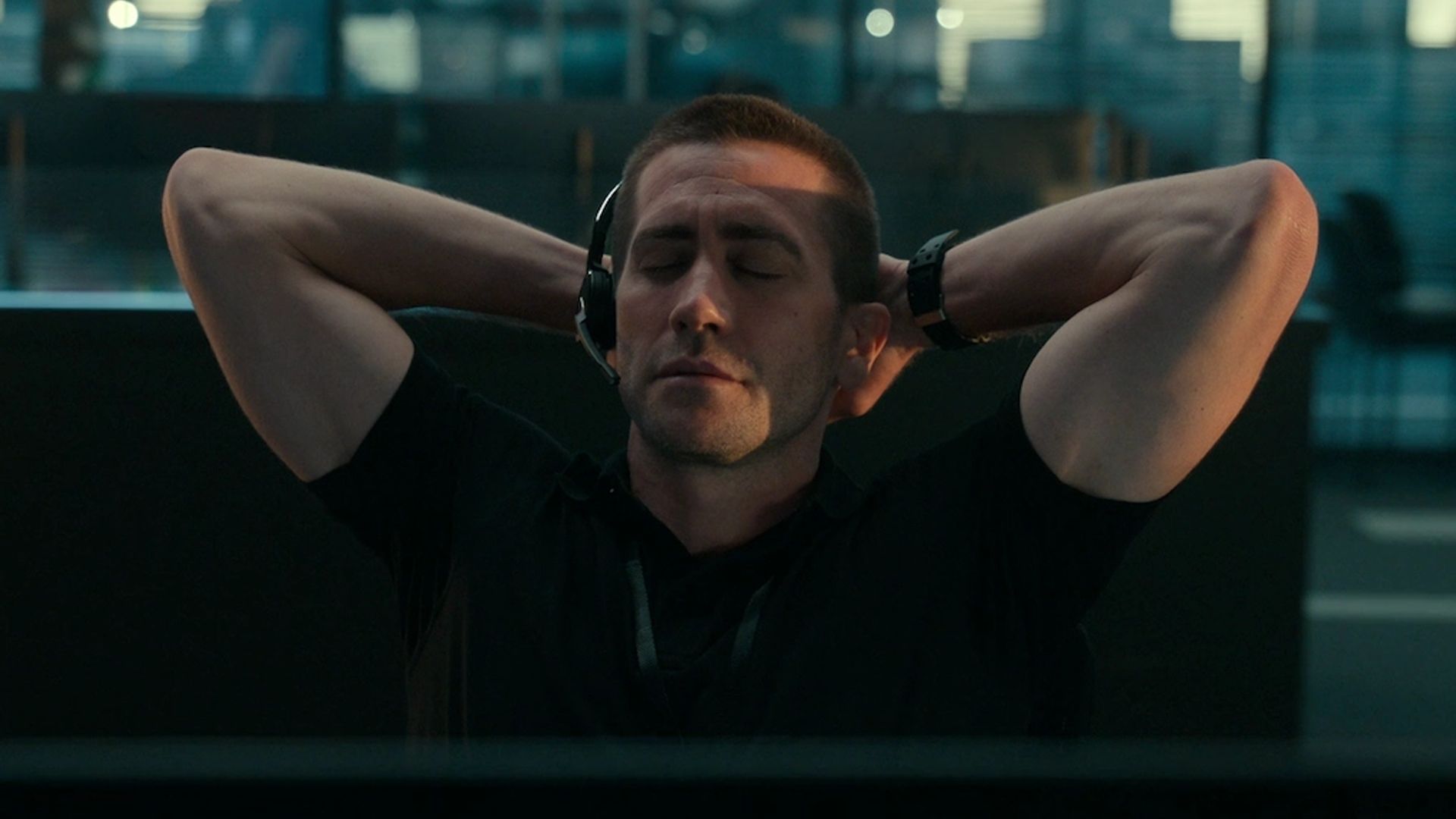 Jake Gyllenhaal con auriculares y micrófono se sienta con los ojos cerrados, las manos detrás de la cabeza