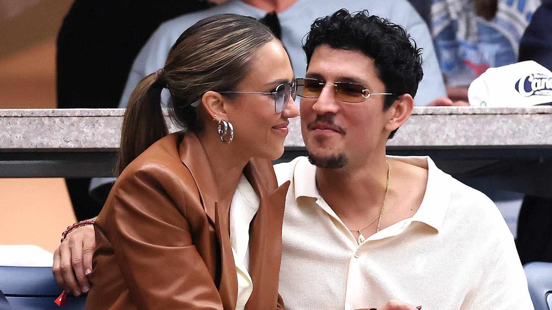 Jessica Alba y Danny Ramírez sentados en las gradas de un evento deportivo abrazándose