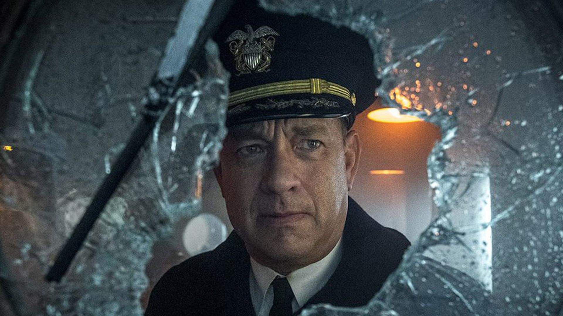 Tom Hanks con uniforme de capitán mira a través de un cristal roto con expresión seria en su rostro