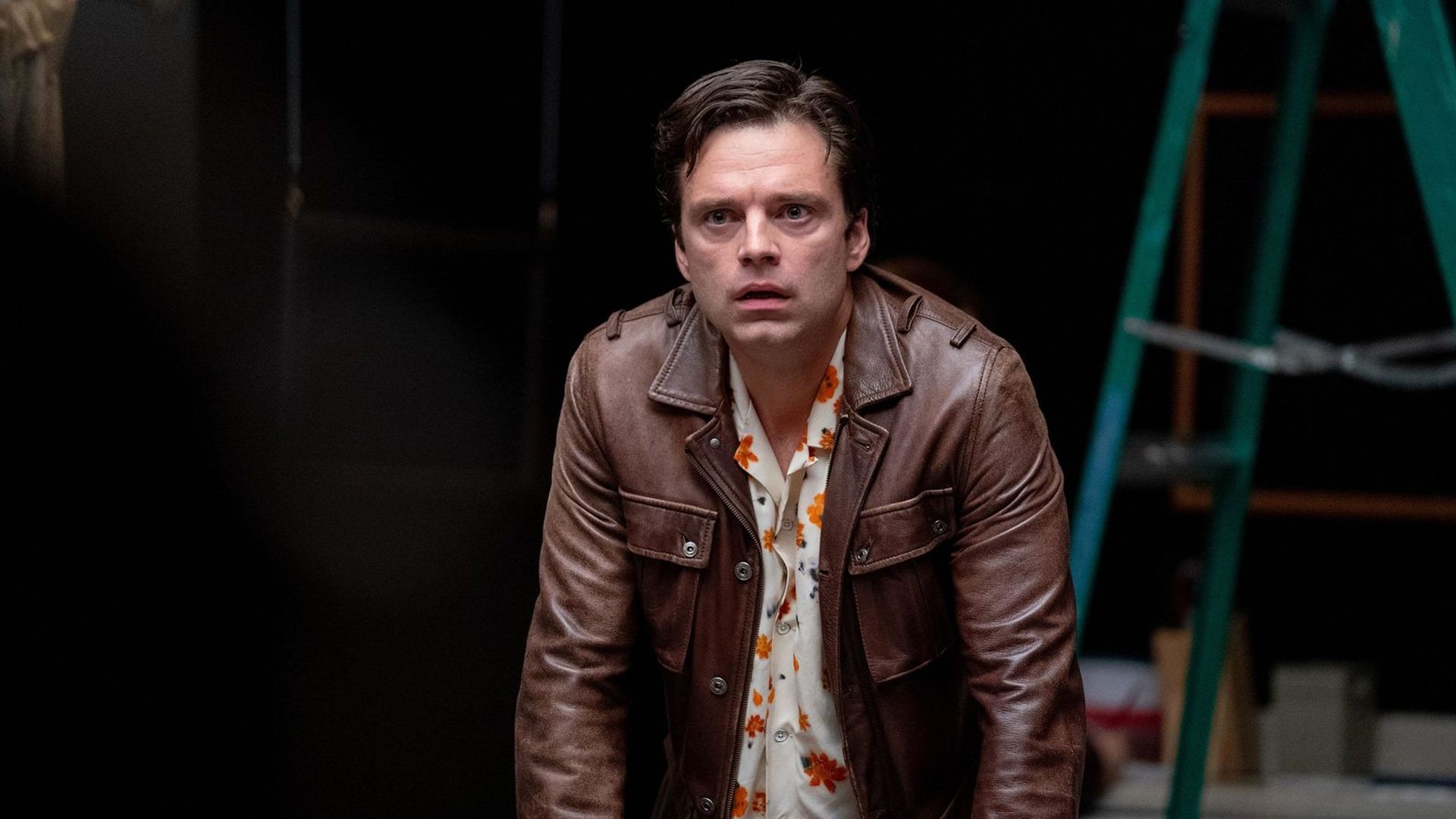 Sebastian Stan con una chaqueta marrón mirando hacia adelante contra un fondo negro