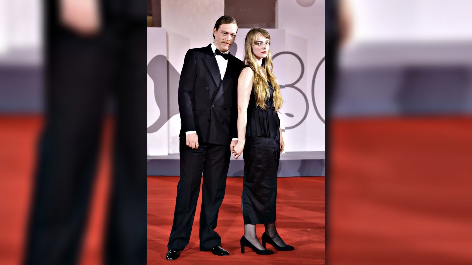 Caleb Landry Jones y Katya Zvereva con trajes de gala posan en la alfombra roja tomados de la mano
