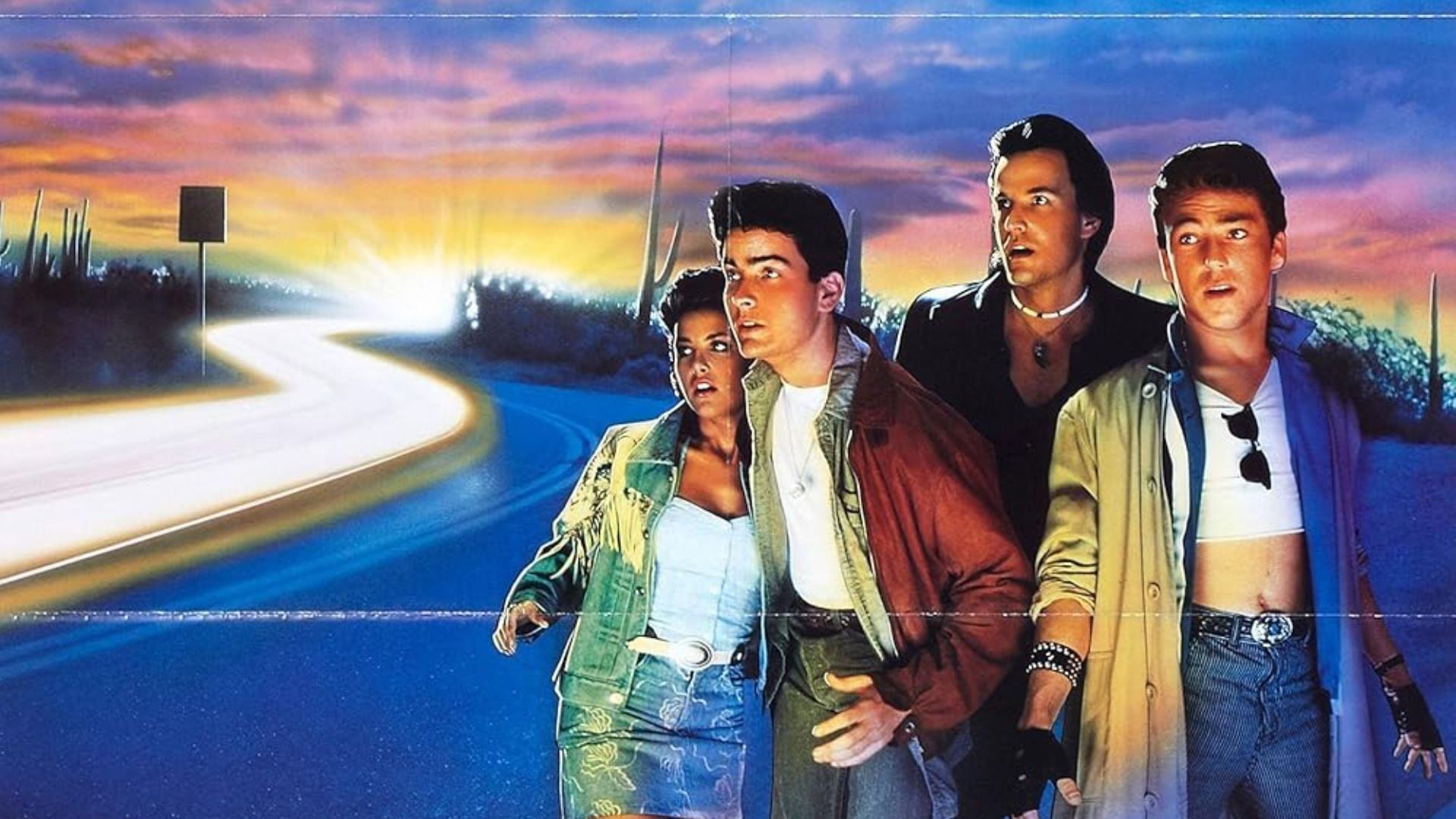 El actor Charlie Sheen con chaqueta roja de pie en la carretera con una chica y dos hombres