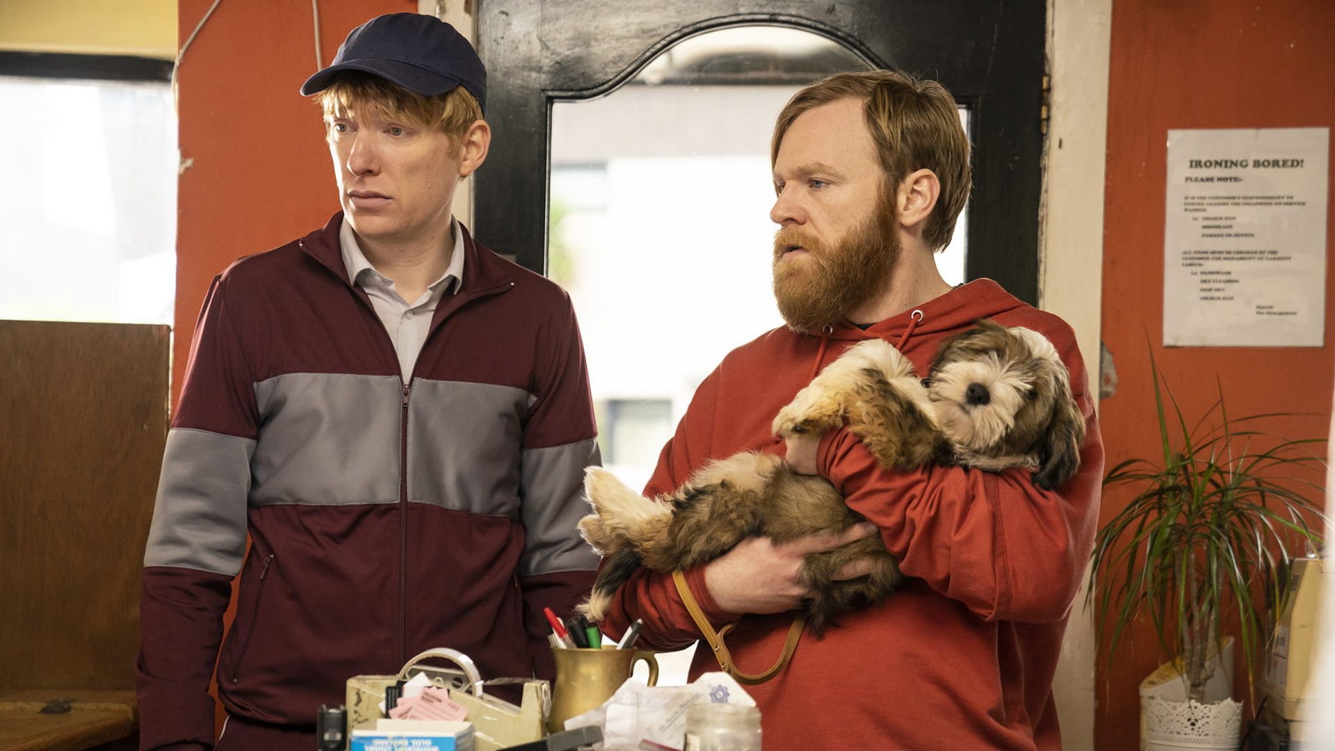 Brian y Domhnall Gleeson en ropa deportiva de pie junto a una mesa mirando hacia un lado