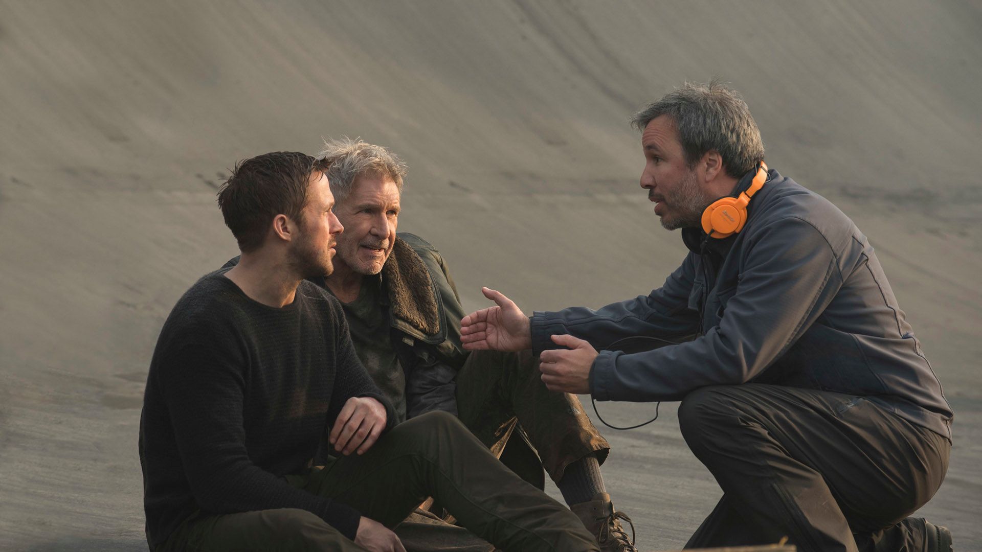 Denis Villeneuve, gesticulando, explica algo a Ryan Gosling y Harrison Ford sentados frente a él