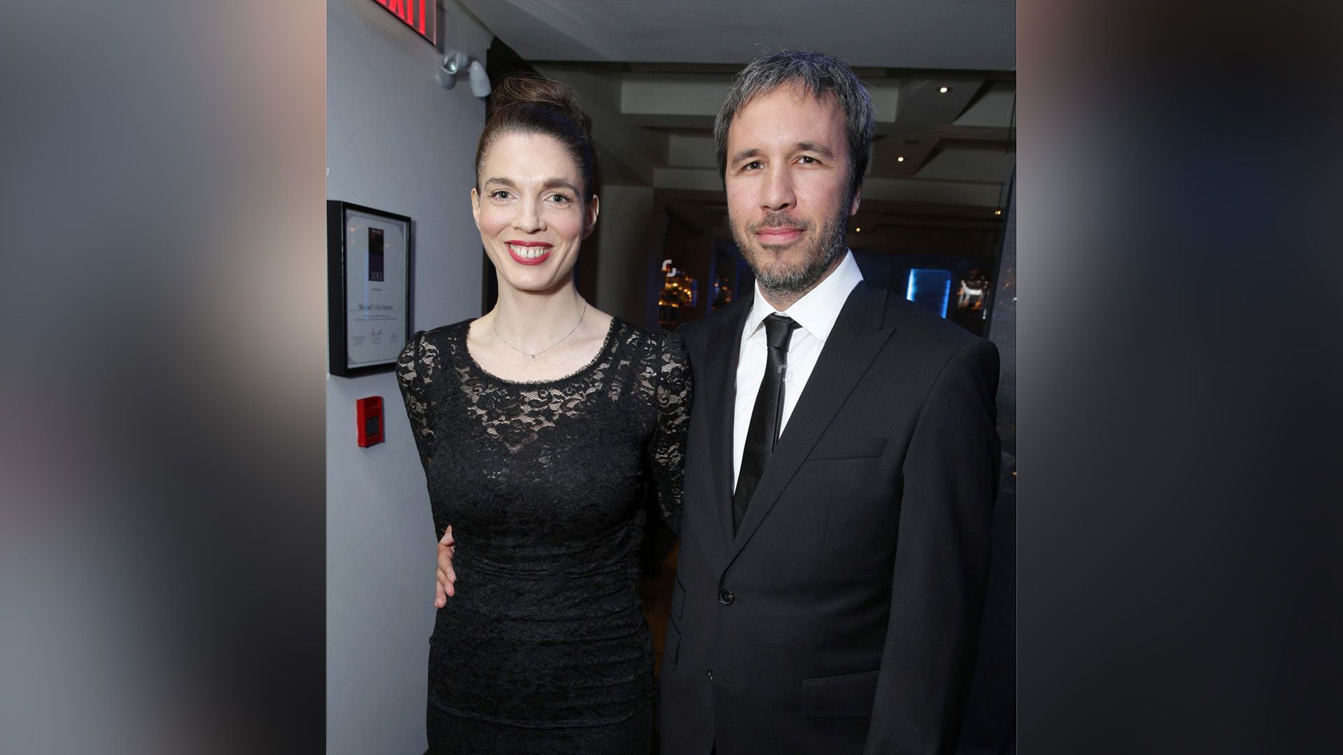 Denis Villeneuve con traje abraza por la cintura a una sonriente Masha Grenon vestida con un vestido negro de encaje