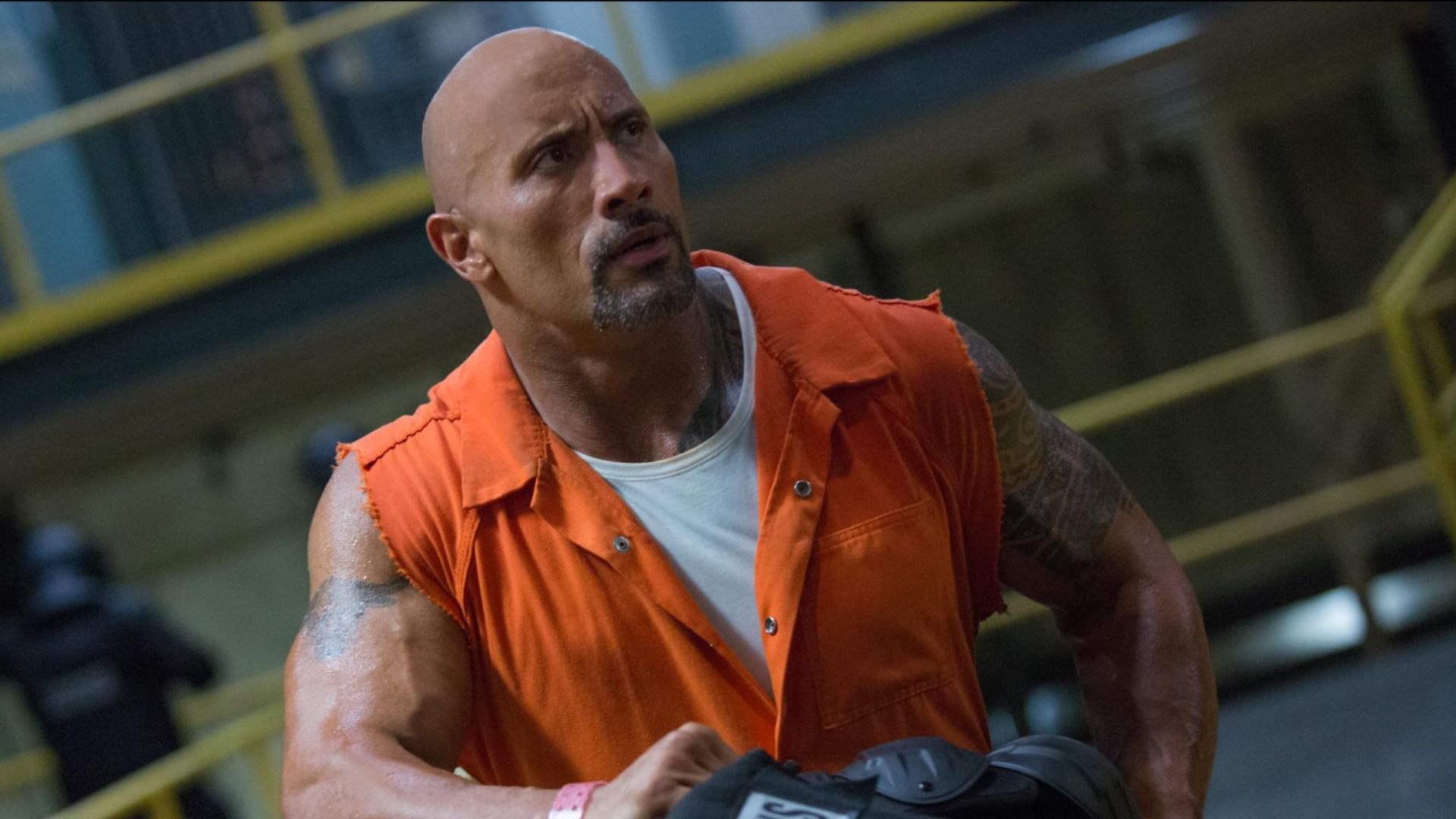 El actor Dwayne Johnson con un chaleco naranja sentado frente a celdas de prisión