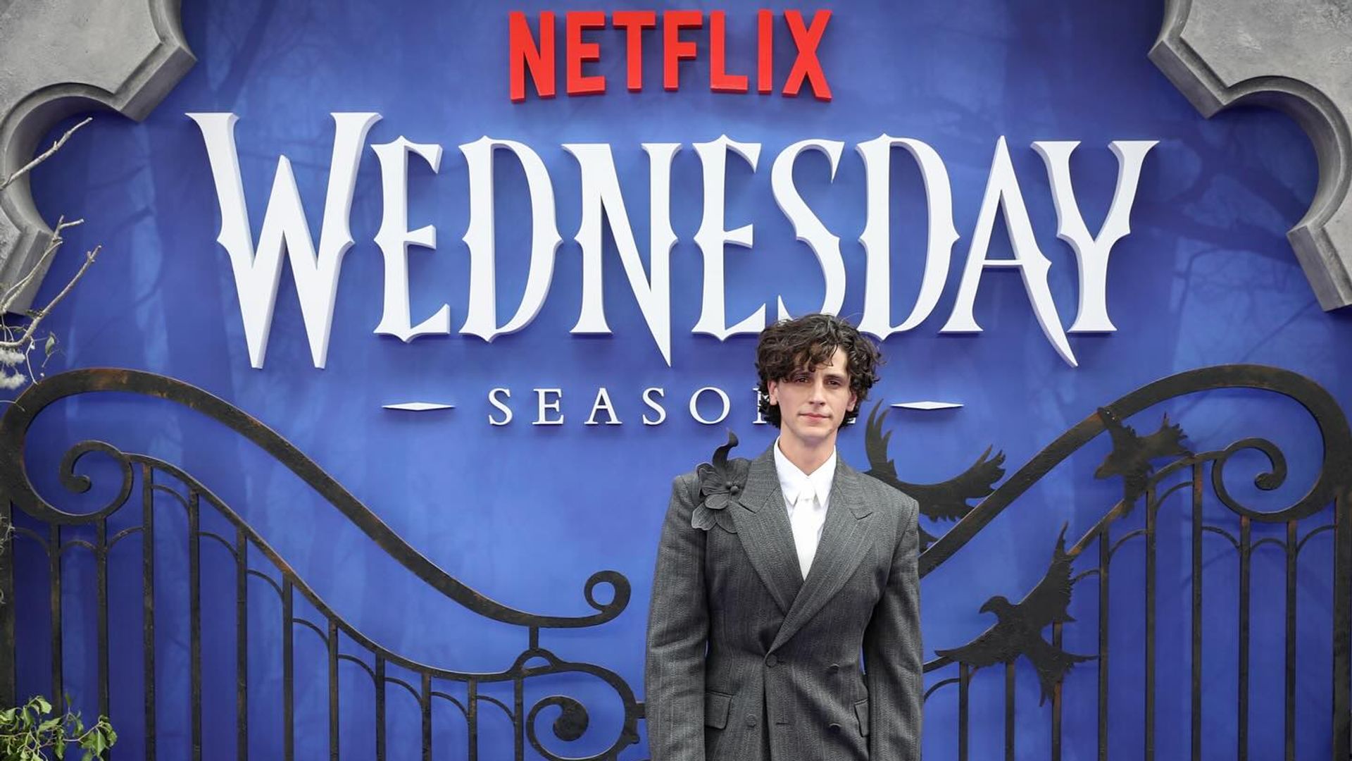 Owen Painter con traje posando contra un fondo de Netflix de Wednesday